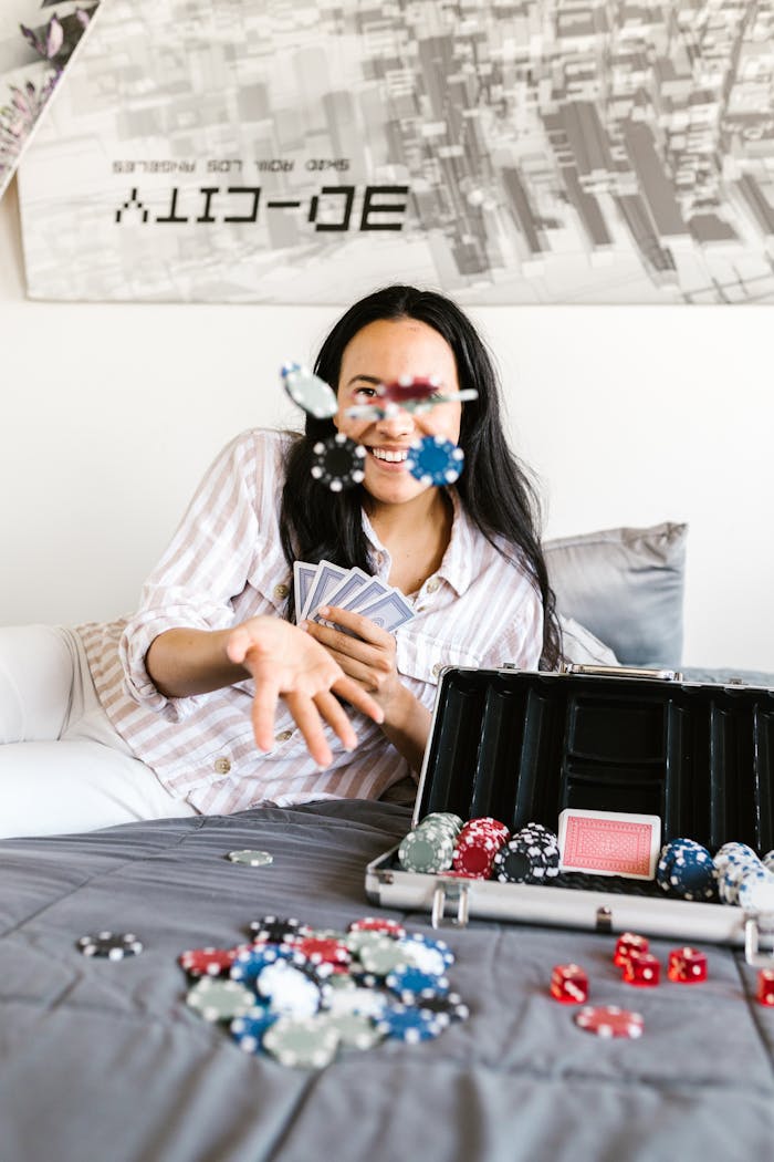 Woman in striped shirt playing poker on bed, tossing chips with cards and poker set.